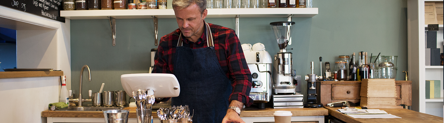 Business owner behind the counter at his cafe looking at the till.